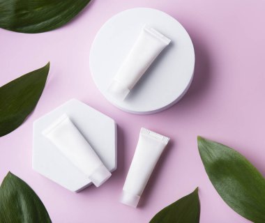 Pembe arka planda yeşil yapraklı beyaz krem tüpleri.