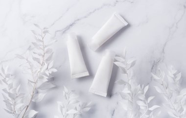 Mermer zemin üzerinde beyaz krem tüpleri ve beyaz yapraklı dekoratif dallar.
