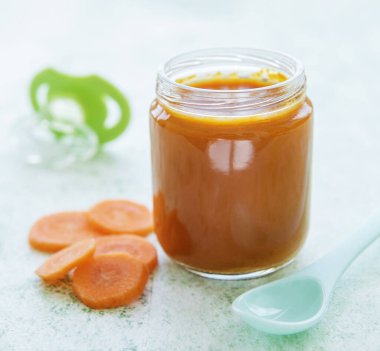 Cam kavanozda kaşıkla ezilmiş bebek havucu, bebek maması.