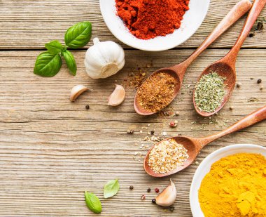 Tahta bir masada, kâselerde ve kaşıklarda çeşitli renklerde baharatlar var.