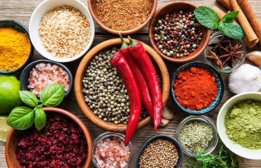 Tahta bir masada, kâselerde ve kaşıklarda çeşitli renklerde baharatlar var.