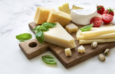 Beyaz mermer arka planda çeşitli peynir, üzüm ve atıştırmalıklar var.