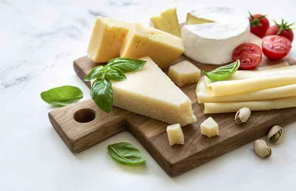 Beyaz mermer arka planda çeşitli peynir, üzüm ve atıştırmalıklar var.