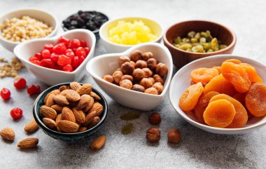 Gri beton arka planda çeşitli kurutulmuş meyve ve fındıklı kaseler.