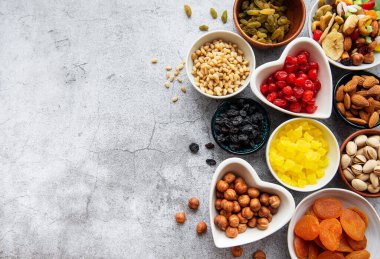 Gri beton arka planda çeşitli kurutulmuş meyve ve fındıklı kaseler.