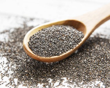 Beyaz ahşap arka planda süslenmiş tahta kaşıkta Chia tohumları.
