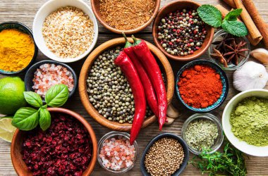 Tahta bir masada, kâselerde ve kaşıklarda çeşitli renklerde baharatlar var.