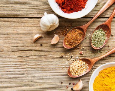 Tahta bir masada, kâselerde ve kaşıklarda çeşitli renklerde baharatlar var.