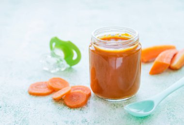 Cam kavanozda kaşıkla ezilmiş bebek havucu, bebek maması.