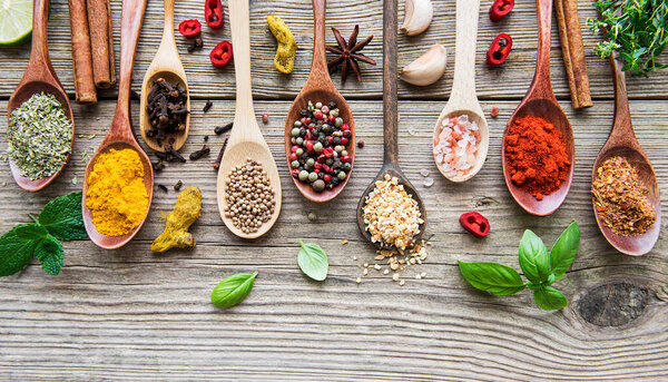 A selection of various colorful spices on a wooden table in  spoons