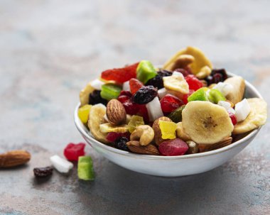 Çeşitli kurutulmuş meyveler ve fındıklar gri beton arka planda.