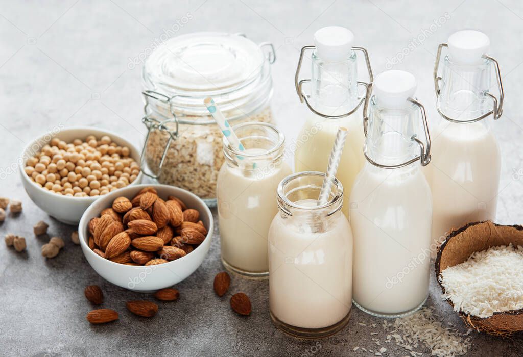 Alternative types of vegan milks in glass bottles on a  concrete background. Top view