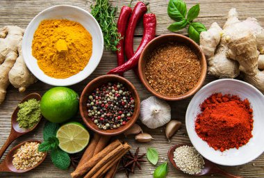 Tahta bir masada, kâselerde ve kaşıklarda çeşitli renklerde baharatlar var.