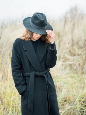 Siyah paltolu ve şapkalı çekici bir kadının portresi. Sonbahar manzarası, kuru otlar..