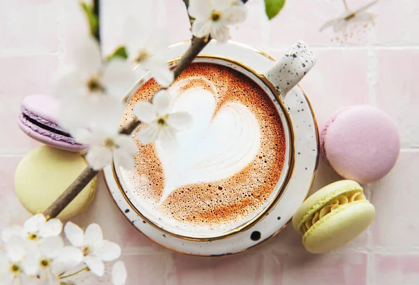 Coffee with a heart-shaped pattern and sweet macaroons desserts on a pink tile background