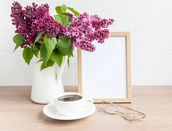 Bouquet of lilac flowers in a vase and empty frame on a wooden table.
