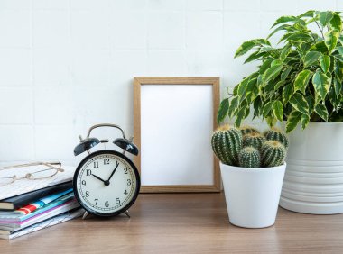 Ofis masasında yığınla not defteri, çalar saat, ofis malzemeleri ve ev bitkileri var.