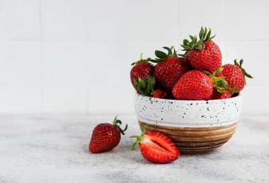 Taze olgun lezzetli çilekler, gri bir arka planda beyaz bir kasede.