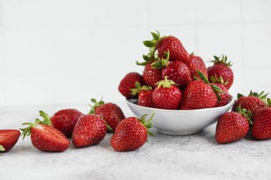 Taze olgun lezzetli çilekler, gri bir arka planda beyaz bir kasede.