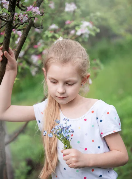 春天花园里的小女孩 手里拿着一朵蓝色的遗忘的花 — 图库照片