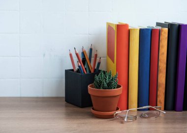 Masaüstünde bir yığın kitap var. Masada çeşitli kitap ve ofis malzemeleri var.