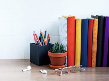 Masaüstünde bir yığın kitap var. Masada çeşitli kitap ve ofis malzemeleri var.