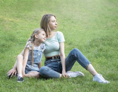 Çimlerin üzerinde oturan ve birlikte eğlenen kadın ve çocuk resmi.