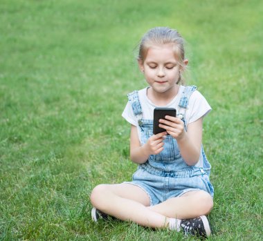 Parkta akıllı telefon kullanan küçük kız.