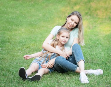 Çimlerin üzerinde oturan ve birlikte eğlenen kadın ve çocuk resmi.