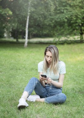 Parkta akıllı telefon kullanan genç bir kadın.