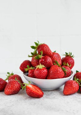 Taze olgun lezzetli çilekler, gri bir arka planda beyaz bir kasede.