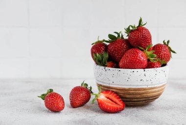 Taze olgun lezzetli çilekler, gri bir arka planda beyaz bir kasede.