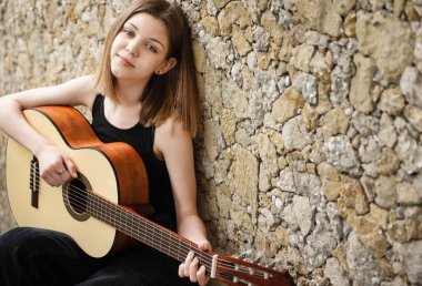 Kahverengi duvarda gitarı olan genç bir kız.