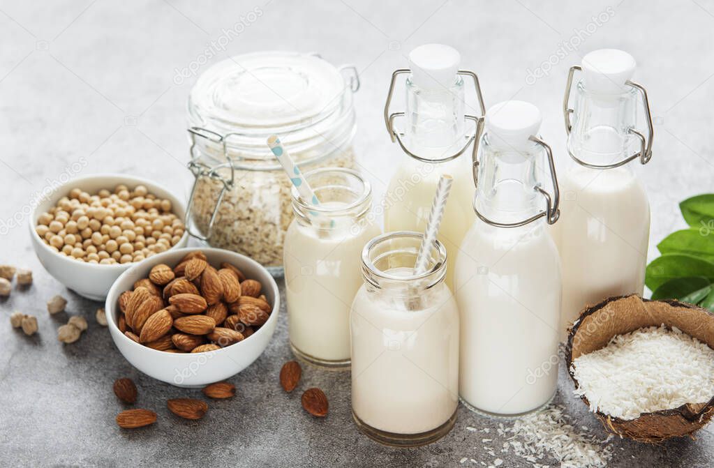 Alternative types of vegan milks in glass bottles on a  concrete background. Top view