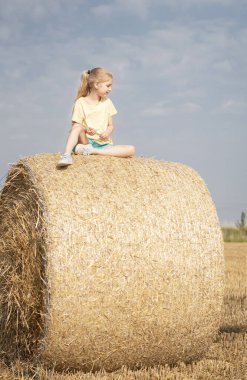 Küçük kız yaz günü buğday tarlasında eğleniyor. Hasat zamanı saman balyasında oynayan çocuk.