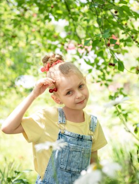 Şirin küçük kız kiraz bahçesindeki bir ağaçtan kiraz topluyor.