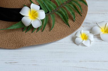 Yaz tatili kavramı. Hasır şapka ve plaj aksesuarları beyaz ahşap arka planda Frangipani çiçekleri