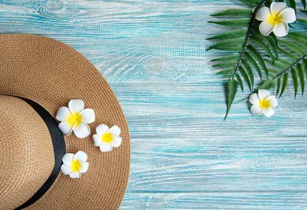 Yaz tatili kavramı. Hasır şapka ve mavi ahşap arka planda frangipani çiçekleri