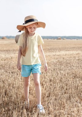 Küçük kız yaz günü buğday tarlasında eğleniyor. Hasat zamanı saman balyasında oynayan çocuk.
