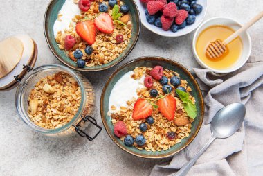 Sağlıklı bir kahvaltı için taze çilek, yabanmersini, ahududu, yoğurt, fındık ve bal dolu granola kaseleri.