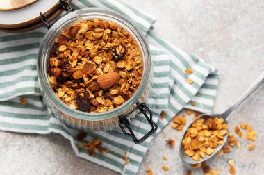 Sağlıklı tahıl gevreğiyle dolu cam kavanoz, bir kaşık havlunun üzerinde karışımı tutuyor.