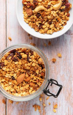 Cam kavanozda yulaf ve fındıklı tahıl gevreği ve tahta arka planda bir kase.