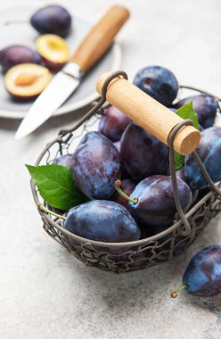 Olgun erikler ve yeşil yapraklar hafif arkaplanda metal bir sepeti dolduruyor.