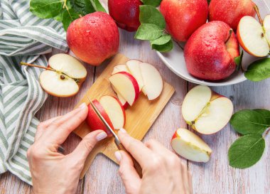 Hands slicing a red apple on a wooden cutting board with more fresh apples around