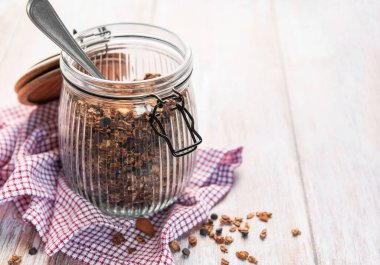 Fındıklı granola, çikolata parçacıkları ve tahta bir masada cam bir kavanozda kaşık.