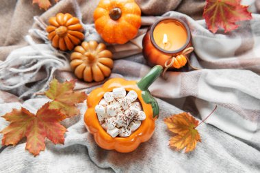 Sıcak kakaolu balkabağı kupası ve sonbahar yapraklı ve mumlu rahat bir battaniyede marşmelov.