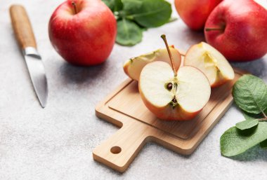 Red apples half sliced on a wooden cutting board with a knife and leaves