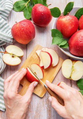 Hands slicing a red apple on a wooden cutting board with more fresh apples around