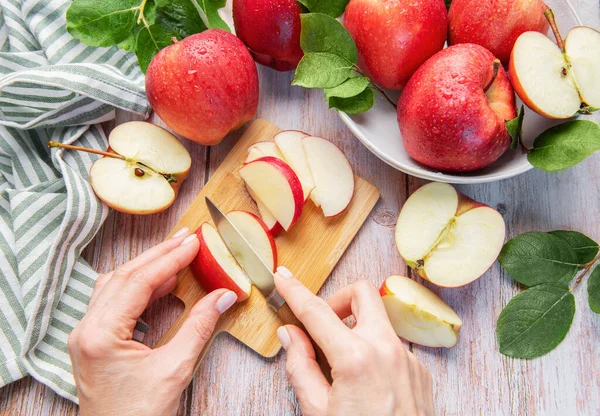 Hands slicing a red apple on a wooden cutting board with more fresh apples around