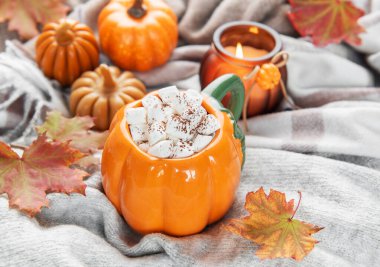 Sıcak kakaolu balkabağı kupası ve sonbahar yapraklı ve mumlu rahat bir battaniyede marşmelov.